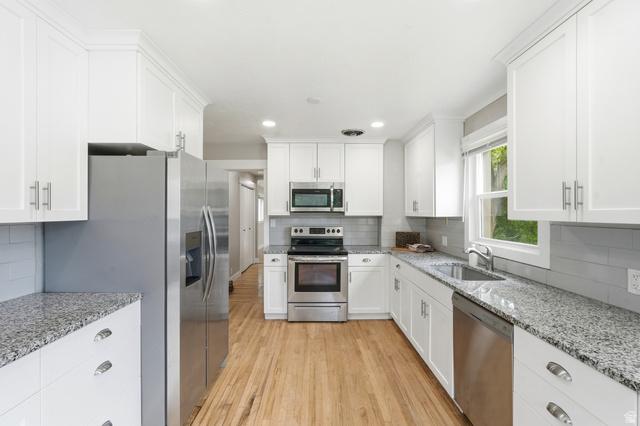 778 East 200 North Logan, UT 84321 - Photo 21 of 43 Kitchen featuring white cabinetry, speckled countertops, stainless steel appliances, wood-finish flooring, and a subway tile backsplash