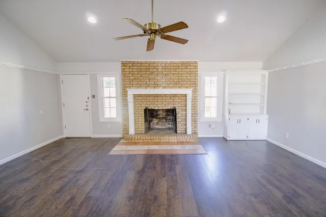an empty room with wooden floor a ceiling fan a fireplace and windows