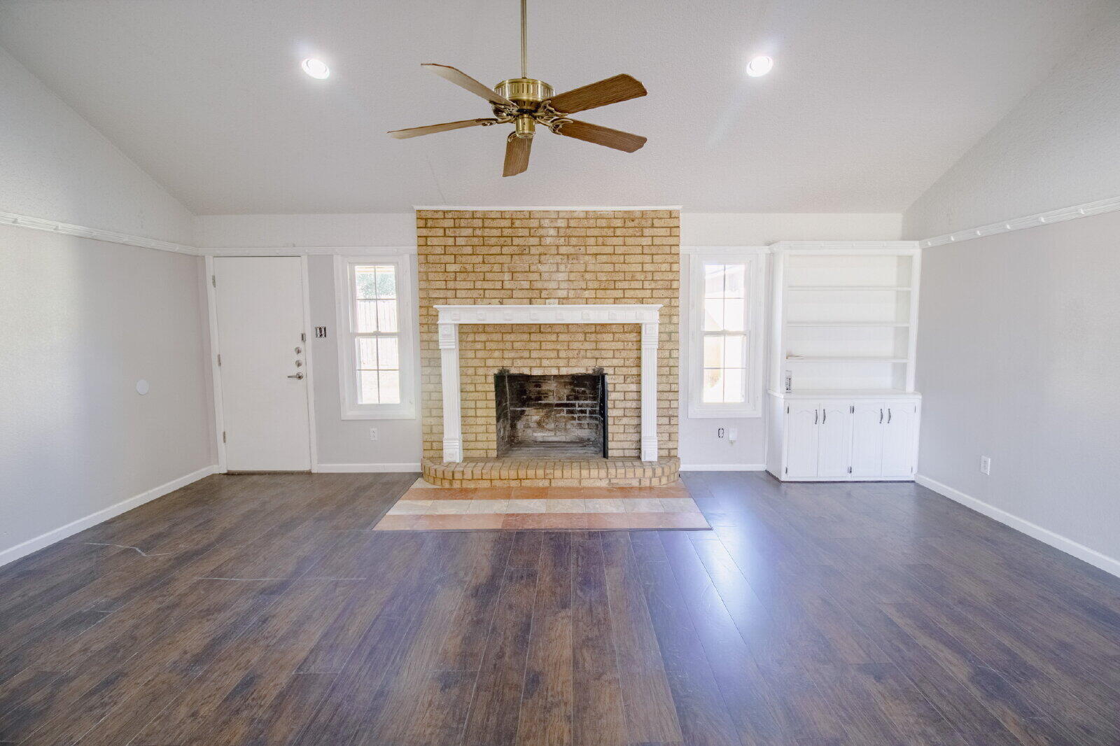 5718 90th Street Lubbock, TX 79424 - Photo 2 of 15 an empty room with wooden floor a ceiling fan a fireplace and windows