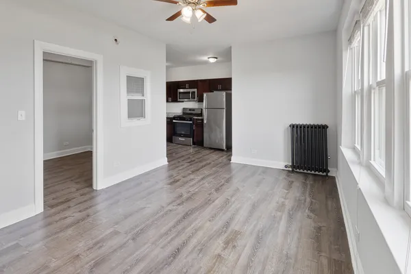 an empty room with wooden floor kitchen view and windows
