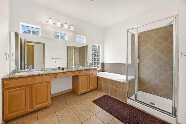 a bathroom with a granite countertop double vanity sink a mirror and a shower