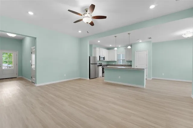 an empty room with wooden floor and kitchen view