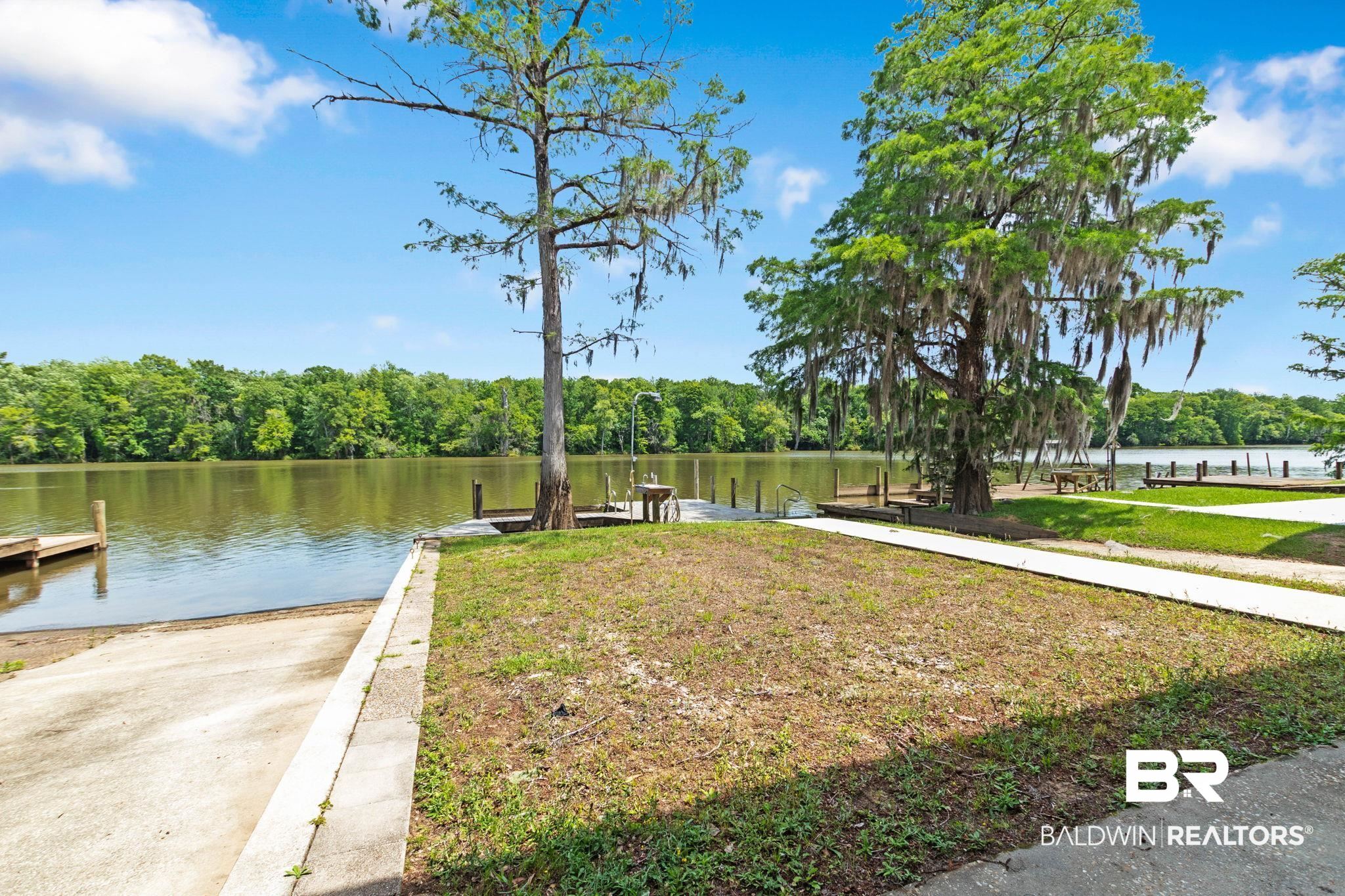 8153 Bryant's Lndg Road Stockton, AL 36579 - Photo 71 of 87 Waterfront property featuring a concrete boat ramp, multiple wooden docks, mature trees, and a substantial body of water bordered by dense foliage