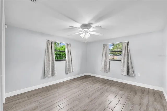 an empty room with wooden floor chandelier fan and windows