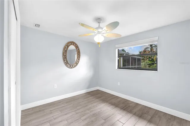 an empty room with wooden floor chandelier fan and windows