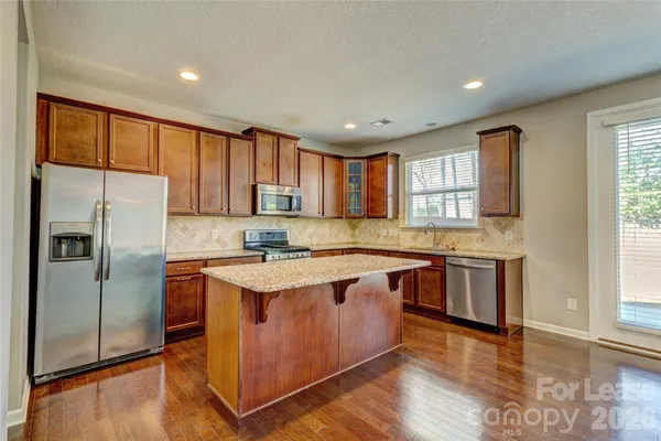 a kitchen with stainless steel appliances granite countertop a refrigerator a sink dishwasher a stove and white countertops with wooden floor