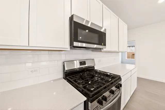 a view of an empty room with kitchen and window