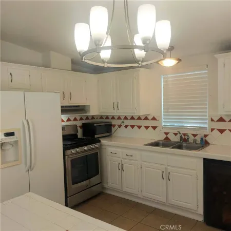 a kitchen with stainless steel appliances a sink a stove a refrigerator cabinets and a chandelier