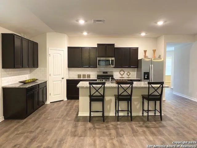 a large kitchen with kitchen island granite countertop a sink and a stove top oven with wooden floor