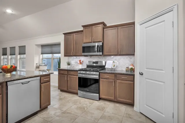 a kitchen with stainless steel appliances granite countertop a stove top oven a sink dishwasher and a refrigerator with wooden cabinets