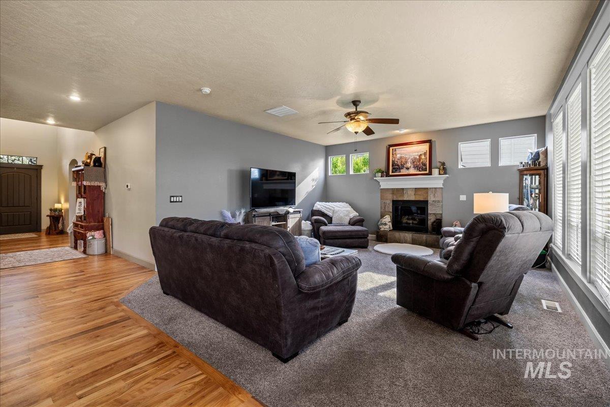 1063 West Hitchcock Street Meridian, ID 83646 - Photo 8 of 50 Living room featuring light wood-style floors, a ceiling fan, a tiled fireplace, and a textured ceiling