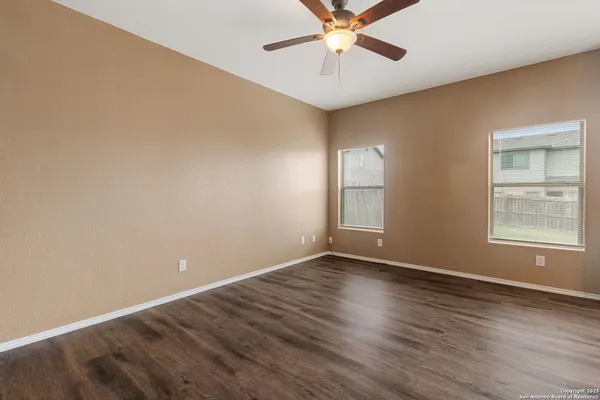 an empty room with wooden floor chandelier fan and windows