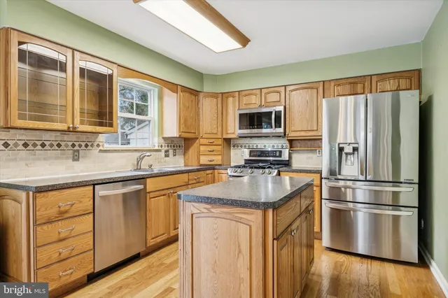 a kitchen with stainless steel appliances granite countertop a refrigerator a sink dishwasher a stove with wooden cabinets and a wooden floor