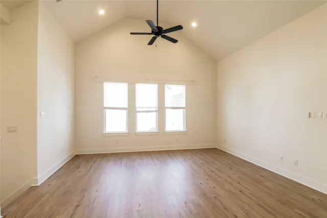 an empty room with wooden floor fan and windows