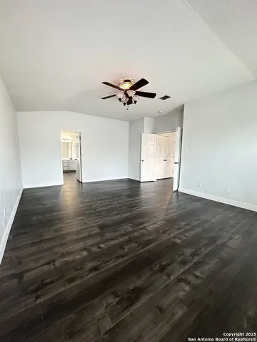 a view of an empty room with chandelier fan and wooden floor