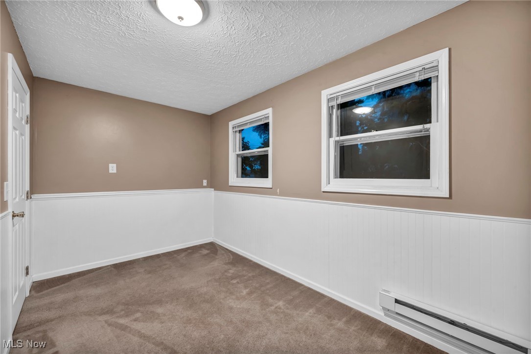 47655 Cooper Foster Park Road Amherst, OH 44001 - Photo 34 of 49 Carpeted empty room with baseboard heating, a textured ceiling, and wainscoting