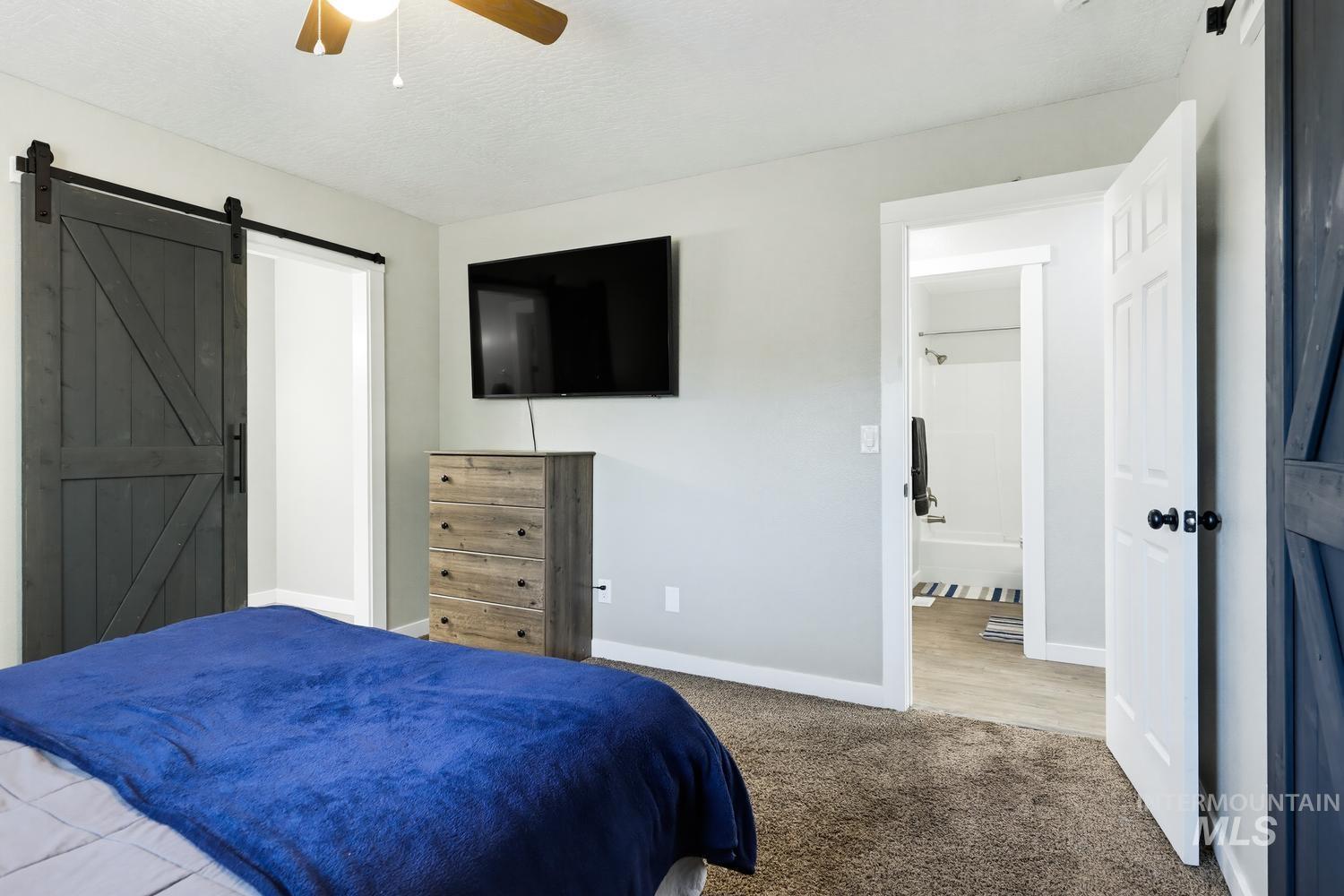 5221 Lockwood Way Caldwell, ID 83607 - Photo 16 of 27 Ceiling fan, dark wood-finish barn door, neutral carpet, light gray wall paint, and white trim