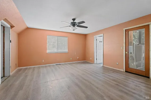 an empty room with wooden floor chandelier fan and windows