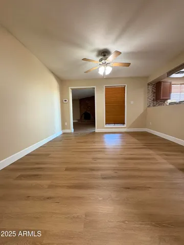 a view of an empty room with wooden floor and a ceiling fan