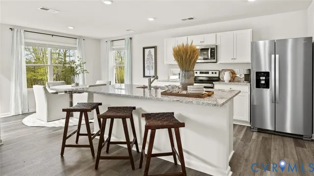 a kitchen with stainless steel appliances granite countertop a stove a refrigerator a sink dishwasher a dining table and chairs with wooden floor