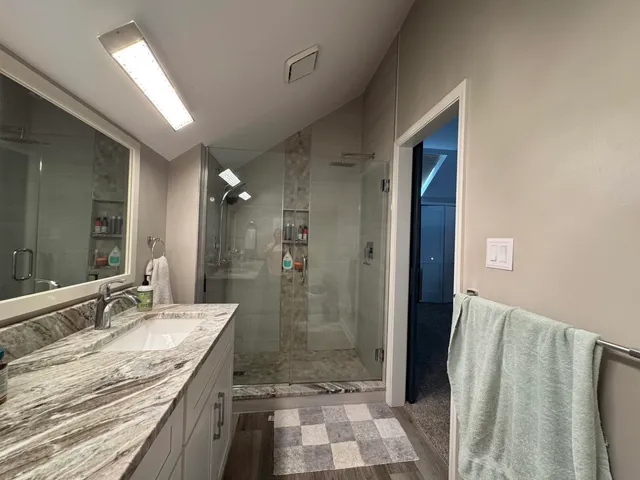 a bathroom with a granite countertop sink a mirror and shower