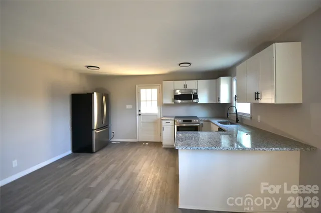 a kitchen with stainless steel appliances granite countertop a refrigerator a sink dishwasher a stove and white countertops with wooden floor