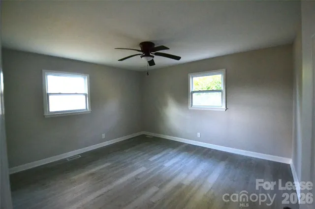 an empty room with wooden floor ceiling fan and windows
