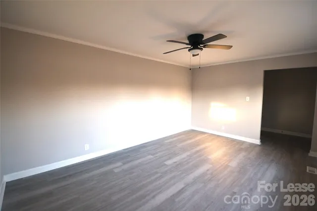 a view of an empty room with wooden floor and a ceiling fan