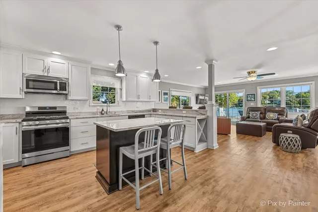 a kitchen with stainless steel appliances kitchen island granite countertop a stove a sink a oven a dining table and chairs with wooden floor