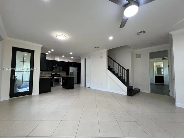 a view of an empty room with kitchen and window