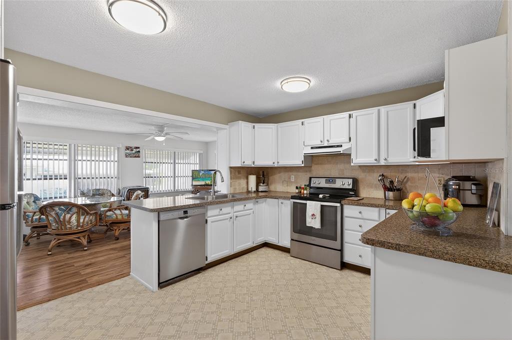 9238 140th Lane Seminole, FL 33776 - Photo 11 of 36 a kitchen with stainless steel appliances granite countertop a stove top oven a sink a dining table and chairs with white cabinets