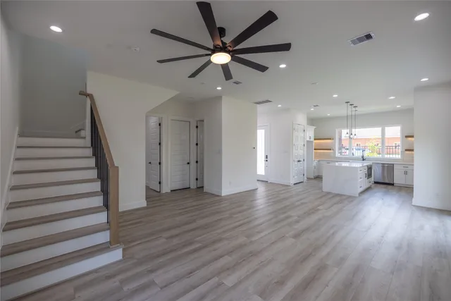 a view of an empty room with wooden floor and a ceiling fan