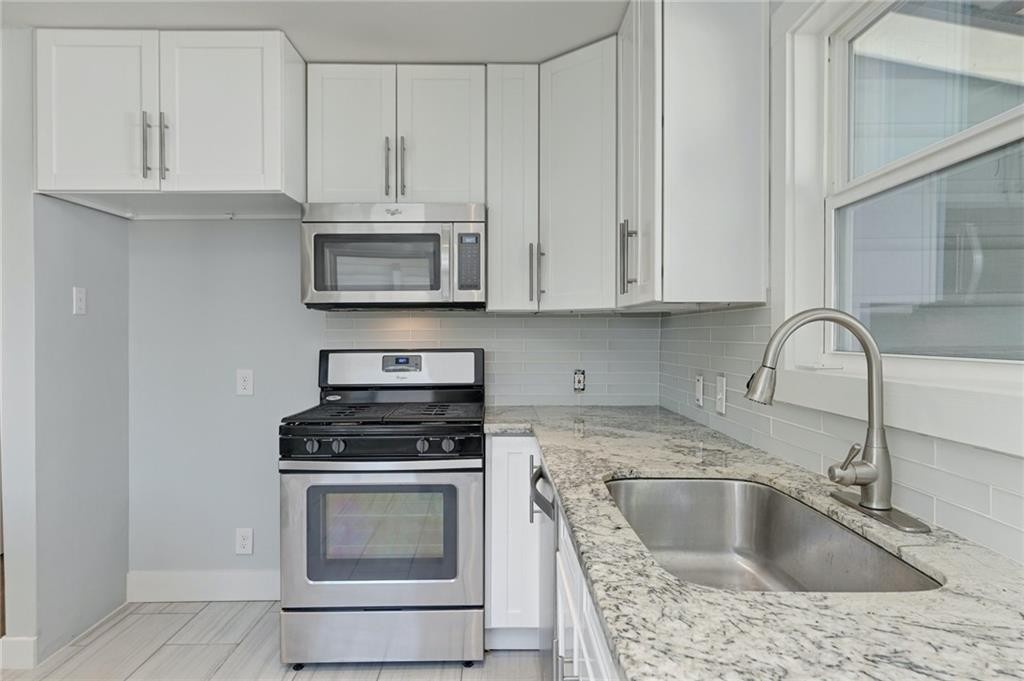 8318 Burrell Drive Austin, TX 78757 - Photo 10 of 27 Kitchen with stainless steel appliances, tasteful backsplash, white cabinets, and light stone counters