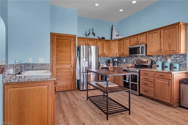 a kitchen with stainless steel appliances granite countertop a stove top oven a sink dishwasher and a refrigerator with wooden cabinets