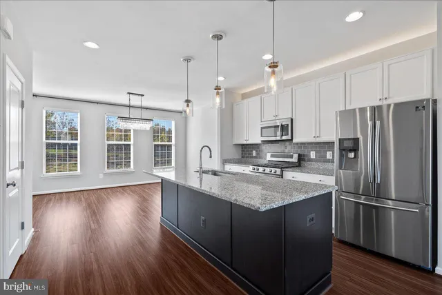 a kitchen with stainless steel appliances granite countertop a refrigerator a sink dishwasher a stove and white countertops with wooden floor