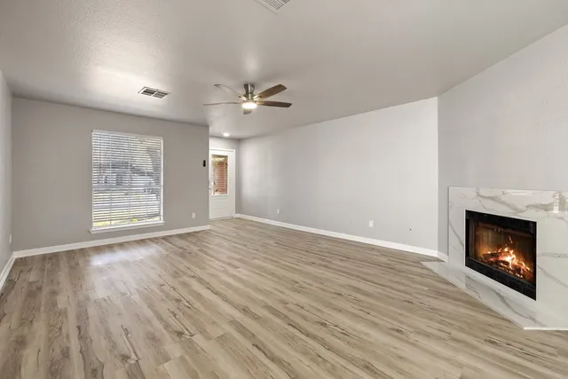 a view of an empty room with wooden floor fireplace and a window