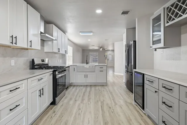 a large kitchen with stainless steel appliances a stove a sink dishwasher a refrigerator and white cabinets with wooden floor