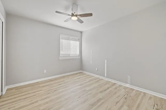 an empty room with wooden floor ceiling fan and windows