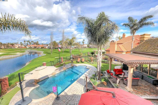 a view of a white house with a swimming pool and a lawn chairs under an umbrella