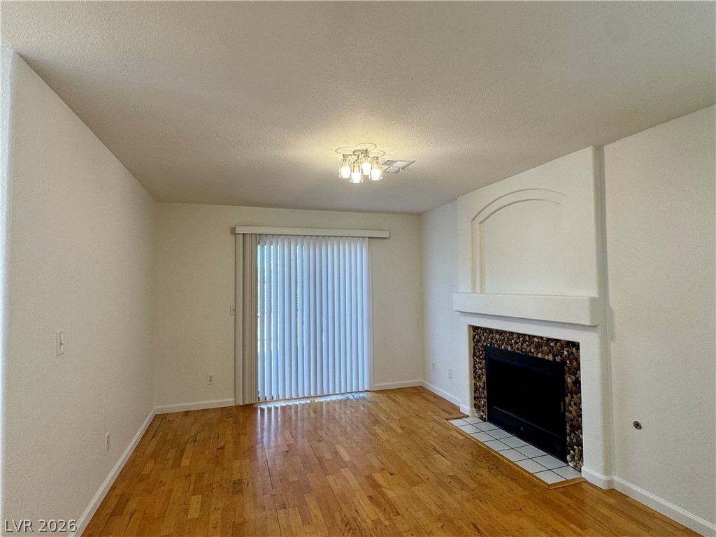 73 Sea Holly Way Henderson, NV 89074 - Photo 50 of 59 Unfurnished living room with light wood-style floors, a tiled fireplace, and a textured ceiling