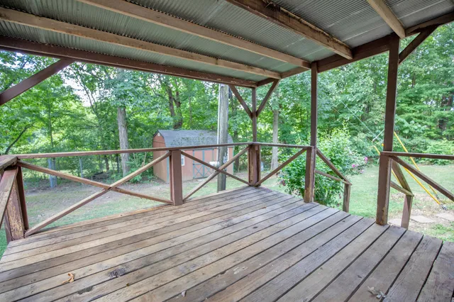 a view of a deck with wooden floor and roof with a garden view