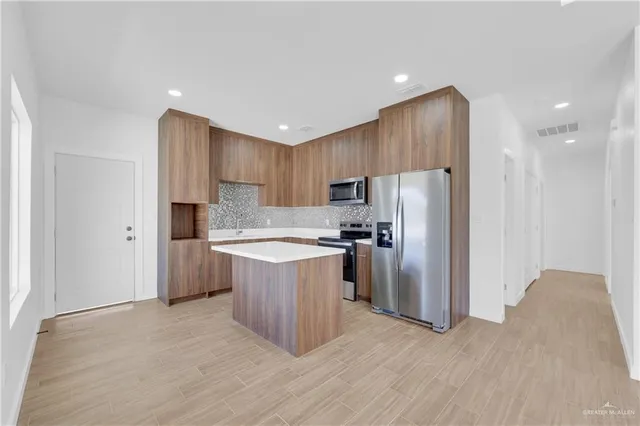 a kitchen with kitchen island granite countertop wooden cabinets a refrigerator and a sink