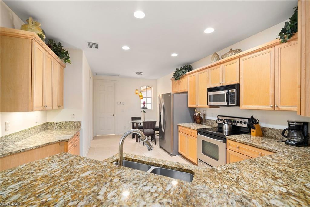 8519 Chase Preserve Drive Naples, FL 34113 - Photo 8 of 29 a kitchen with stainless steel appliances granite countertop a stove top oven a sink a dining table and chairs with wooden floor