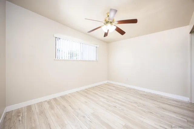 an empty room with wooden floor fan and windows
