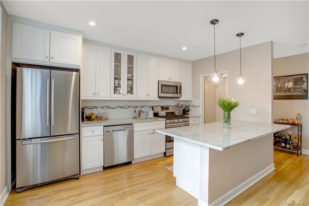 a kitchen with stainless steel appliances granite countertop a refrigerator a sink dishwasher a stove top oven a refrigerator with white cabinets and wooden floor