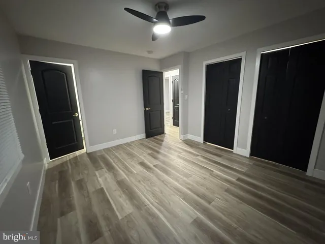 a view of an empty room with wooden floor and a ceiling fan
