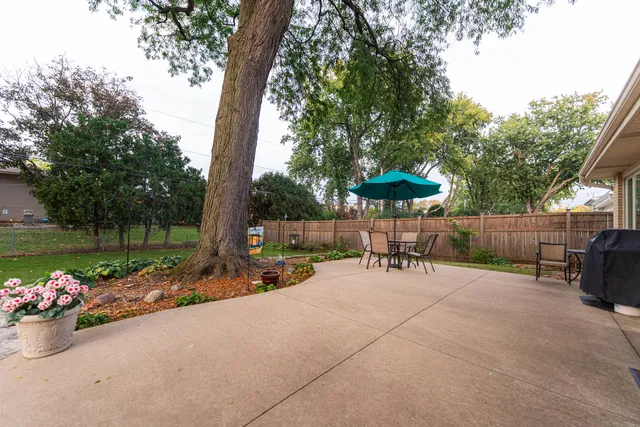a view of a patio with a table and chairs under an umbrella with a small garden