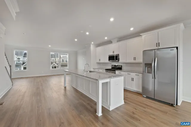 a kitchen with stainless steel appliances granite countertop a refrigerator a stove a sink and white cabinets with wooden floor