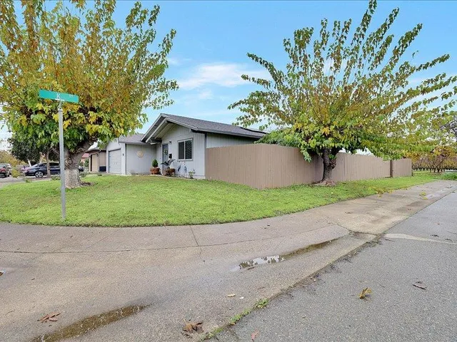 a white house with a big yard plants and large trees