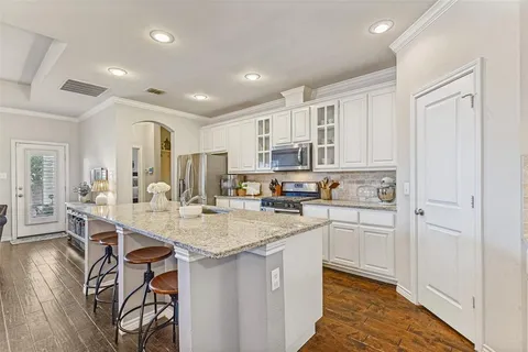 a kitchen with stainless steel appliances granite countertop a kitchen island a stove a sink a refrigerator and white cabinets with wooden floor